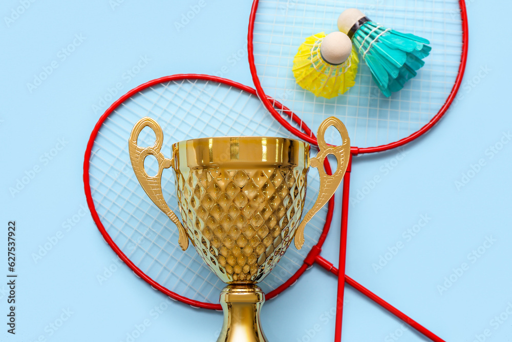 Gold cup with badminton rackets and shuttlecocks on blue background