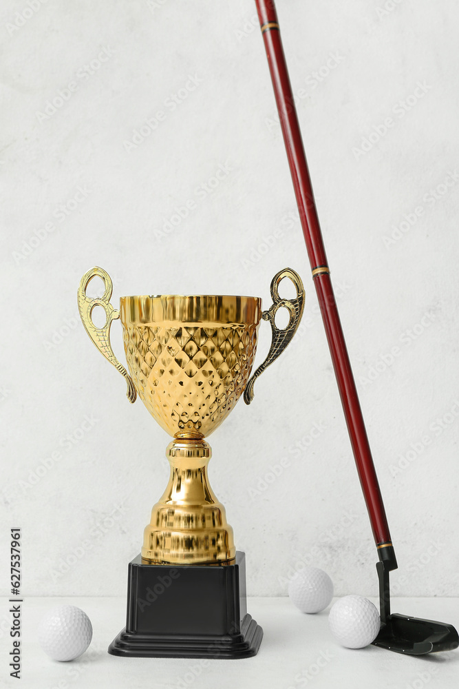 Gold cup with golf club and balls on light background