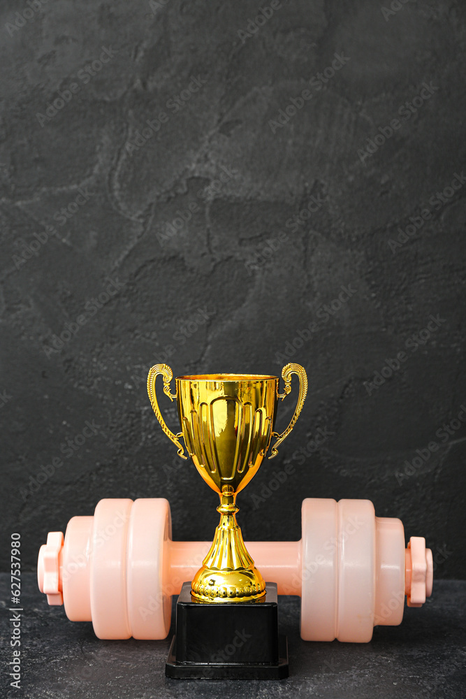 Gold cup with dumbbell on dark background