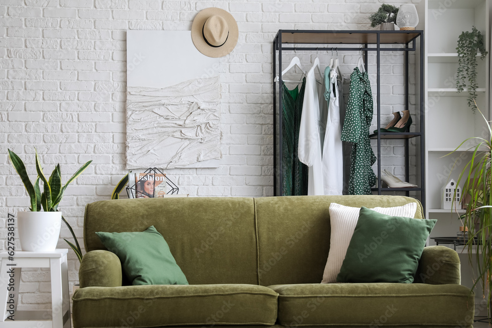 Interior of light room with sofa, shelving unit and clothes