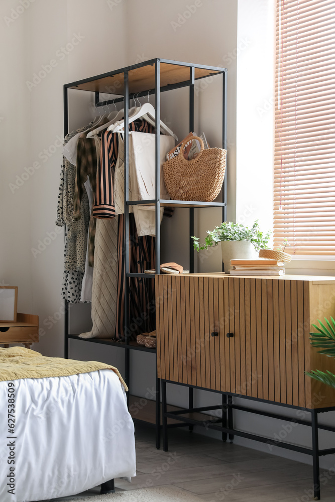 Interior of light bedroom with shelving unit and clothes