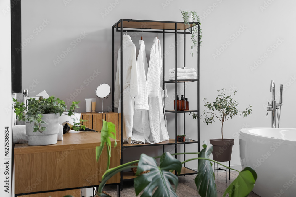 Shelving unit with bathrobes and bath accessories in interior of light room