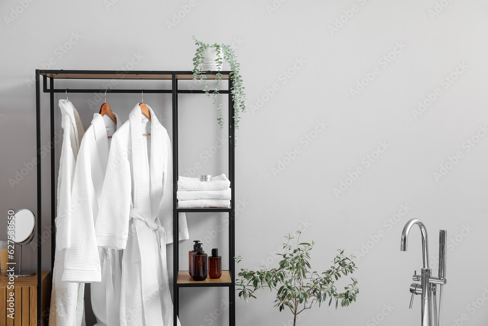 Shelving unit with bathrobes and bath accessories in interior of light room