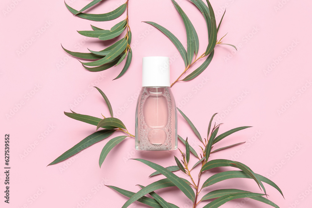 Bottle of micellar water with plant branches on pink background