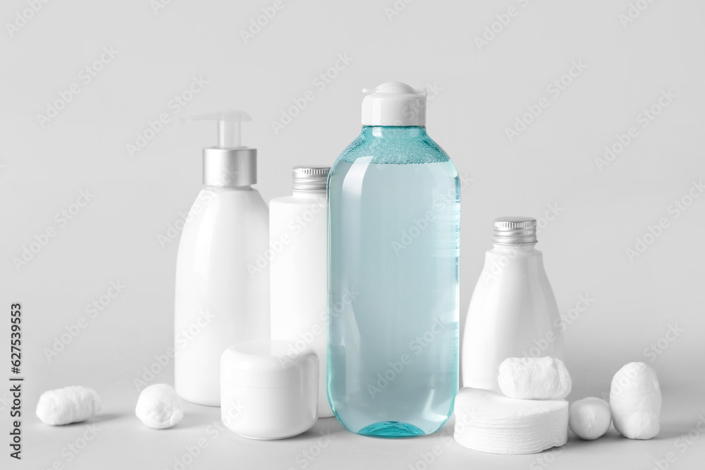 Micellar water with cosmetic products, cotton balls and pads on light background