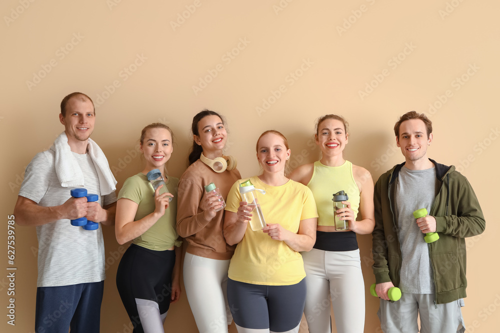 Group of sporty young people with dumbbells and bottles on beige background