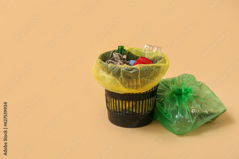 Full trash bin and garbage bag on beige background