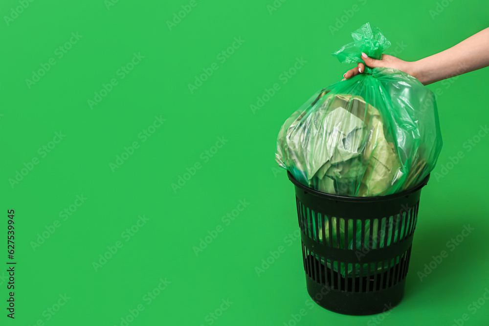 Female hand taking full garbage bag from trash bin on green background