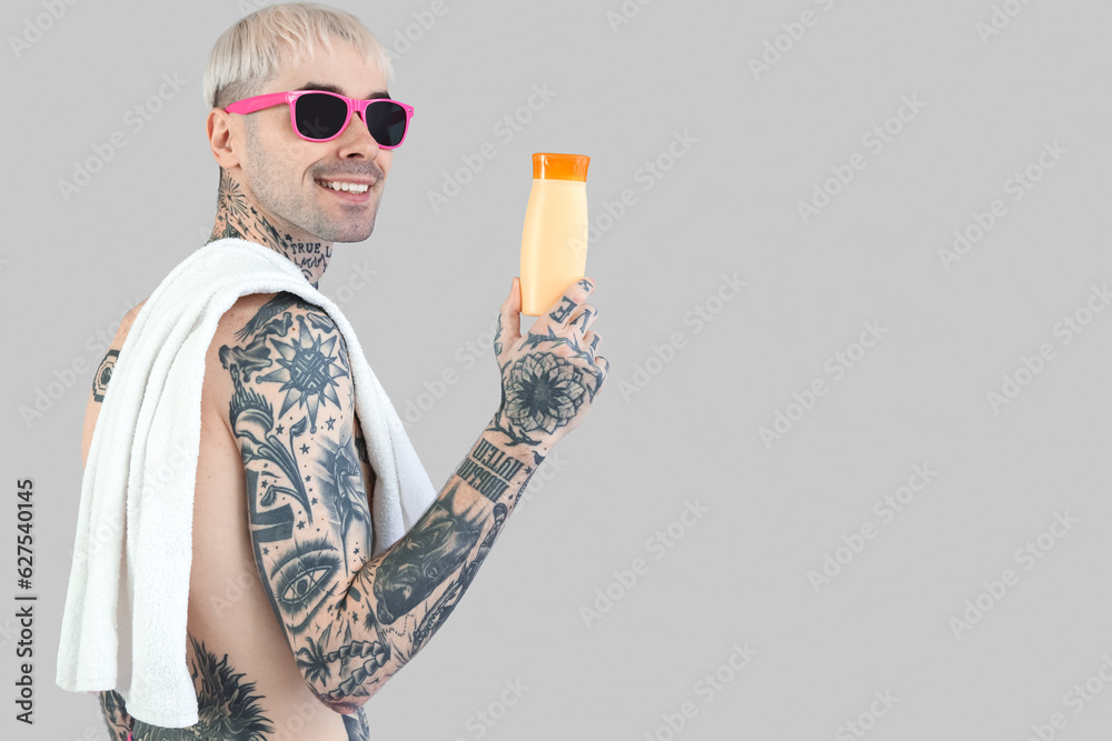 Tattooed man with sunscreen cream on light background