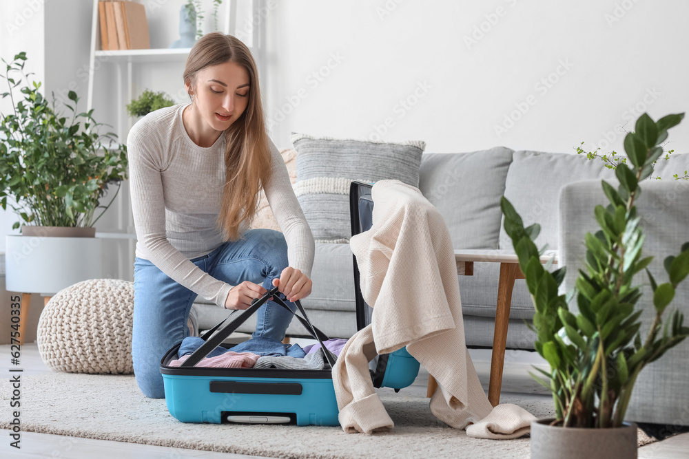 Young woman unpacking suitcase at home