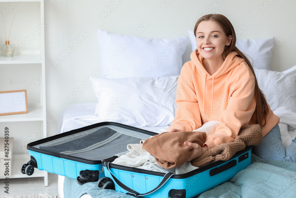 Young woman unpacking her clothes from suitcase in bedroom