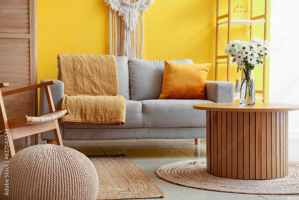 Interior of stylish living room with grey sofa and chrysanthemum flowers on coffee table