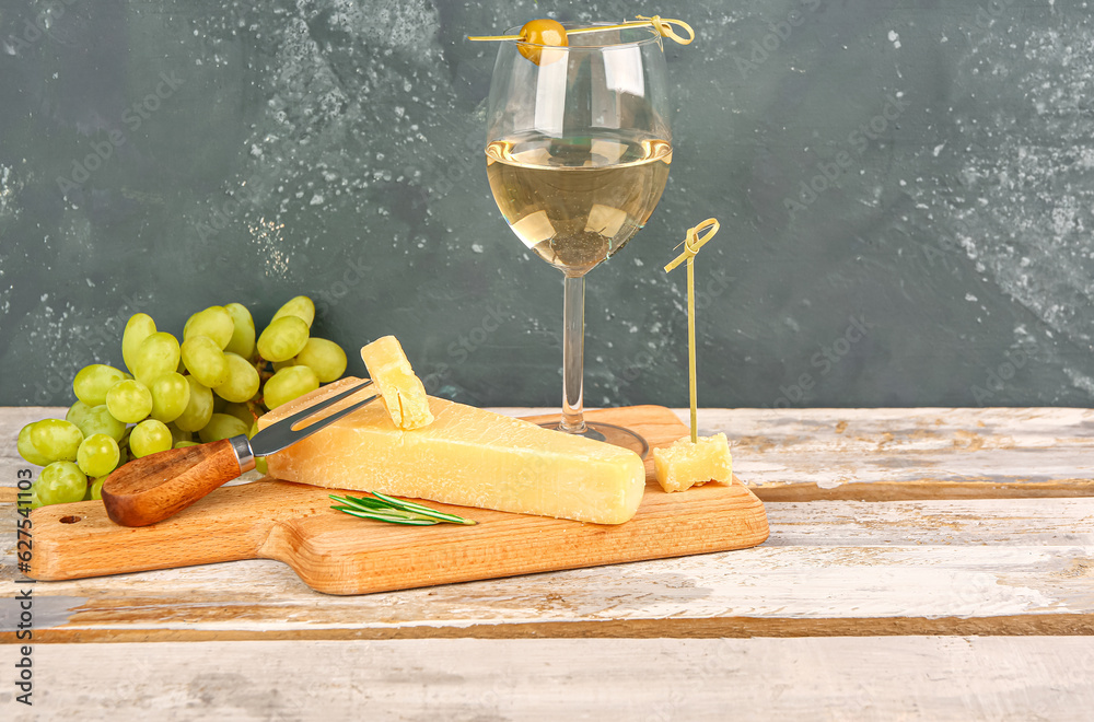 Wooden board with pieces of tasty Parmesan cheese, glass of wine and grapes on table