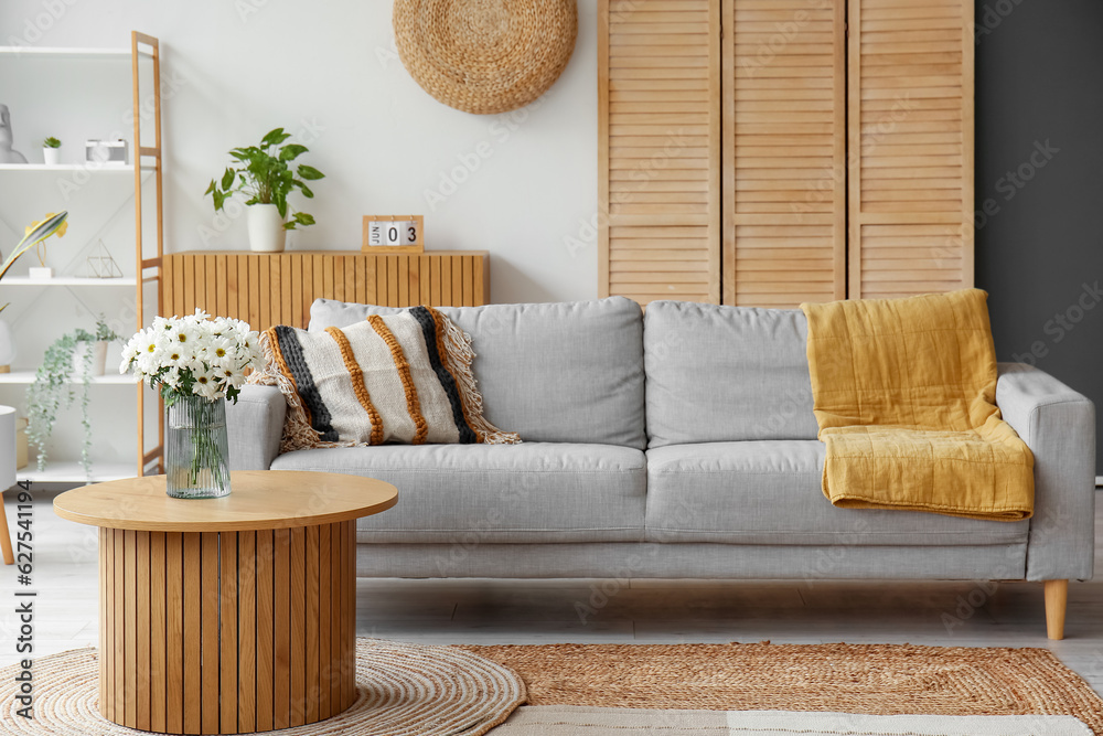 Interior of light living room with grey sofa and wooden coffee table