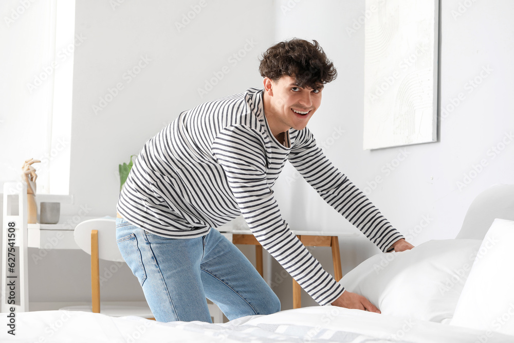 Young man making his bed at home