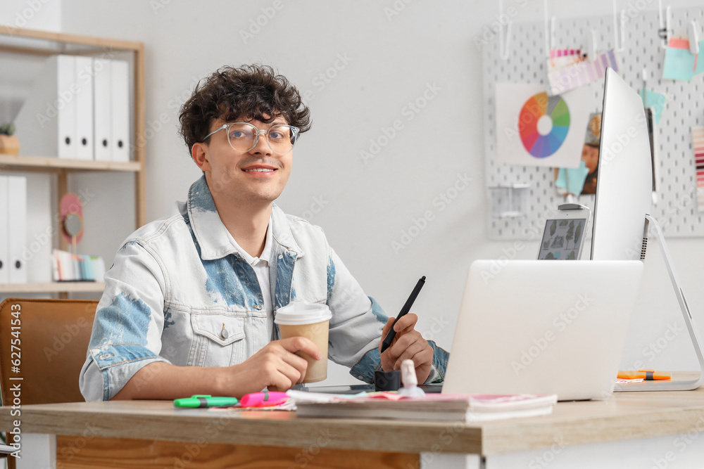 Male graphic designer with cup of coffee working at table in office