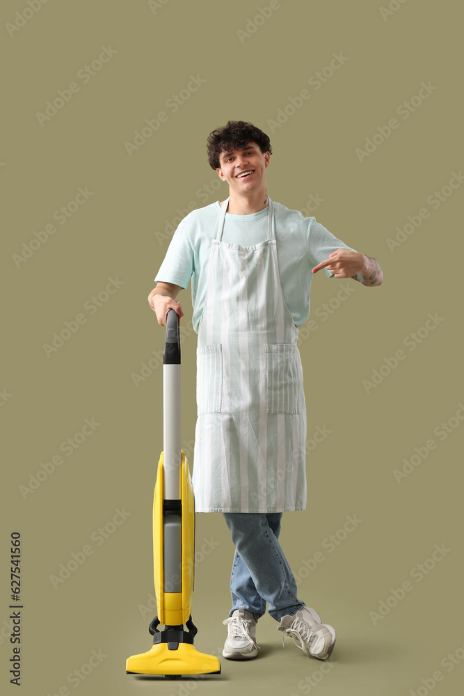 Young man pointing at vacuum cleaner on green background