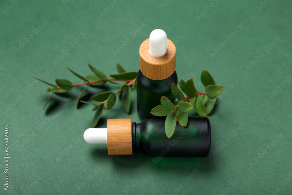 Bottles of cosmetic oil with eucalyptus twigs on dark green background