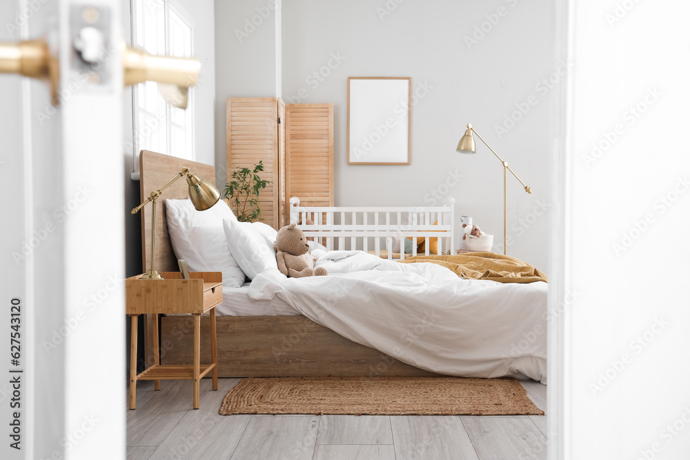 Interior of light bedroom with bed and baby crib