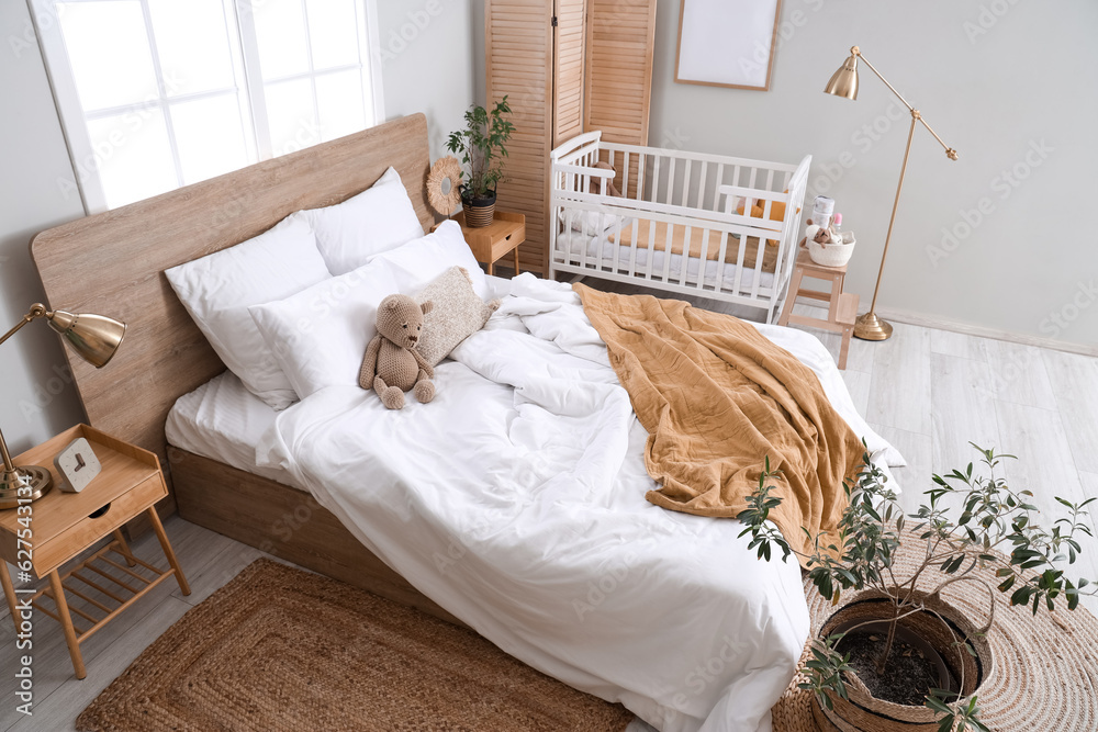 Interior of light bedroom with bed and baby crib