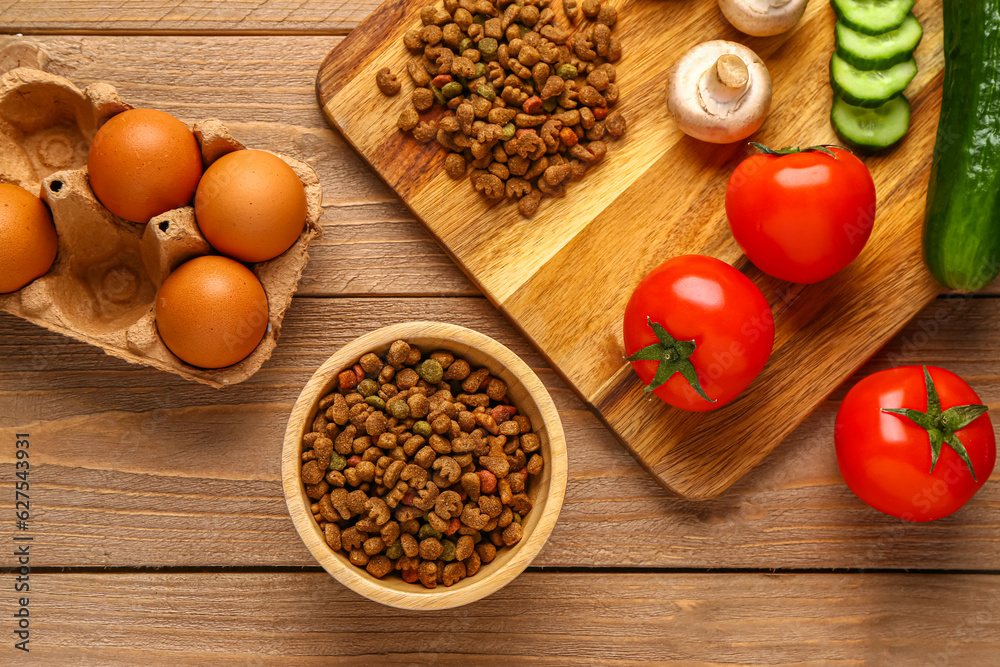 Bowl with dry pet food and natural products on wooden background