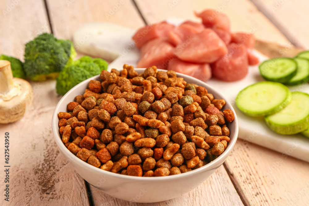 Bowl with dry pet food on light wooden background, closeup