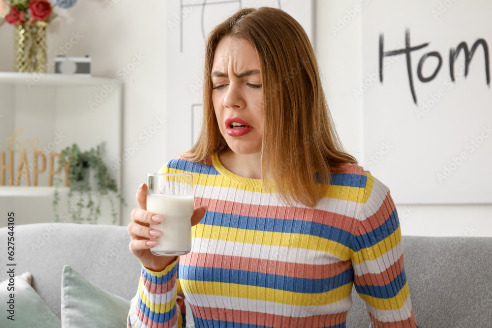 Displeased young woman with glass of milk at home