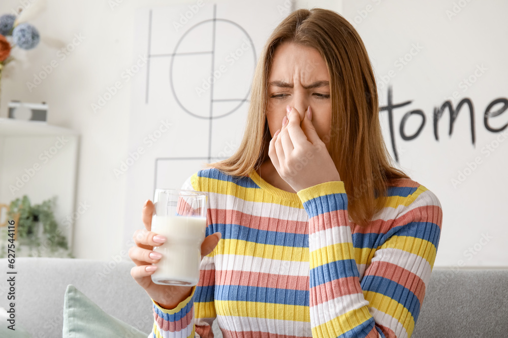 Displeased young woman with glass of milk at home