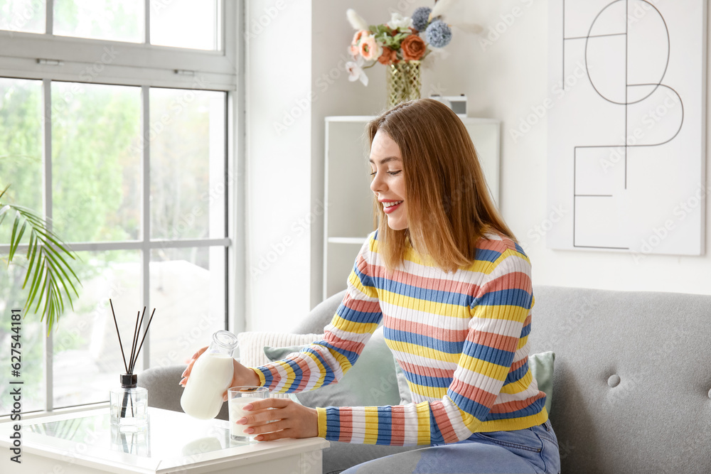 Young woman pouring milk into glass at home