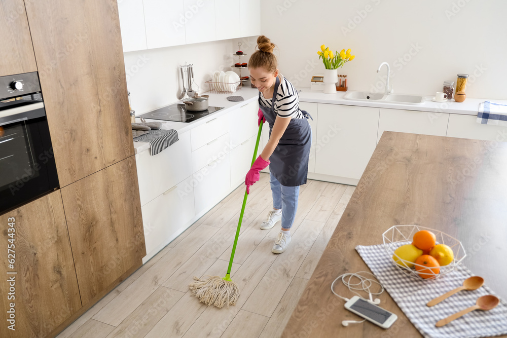 Pretty young woman mopping floor in light kitchen