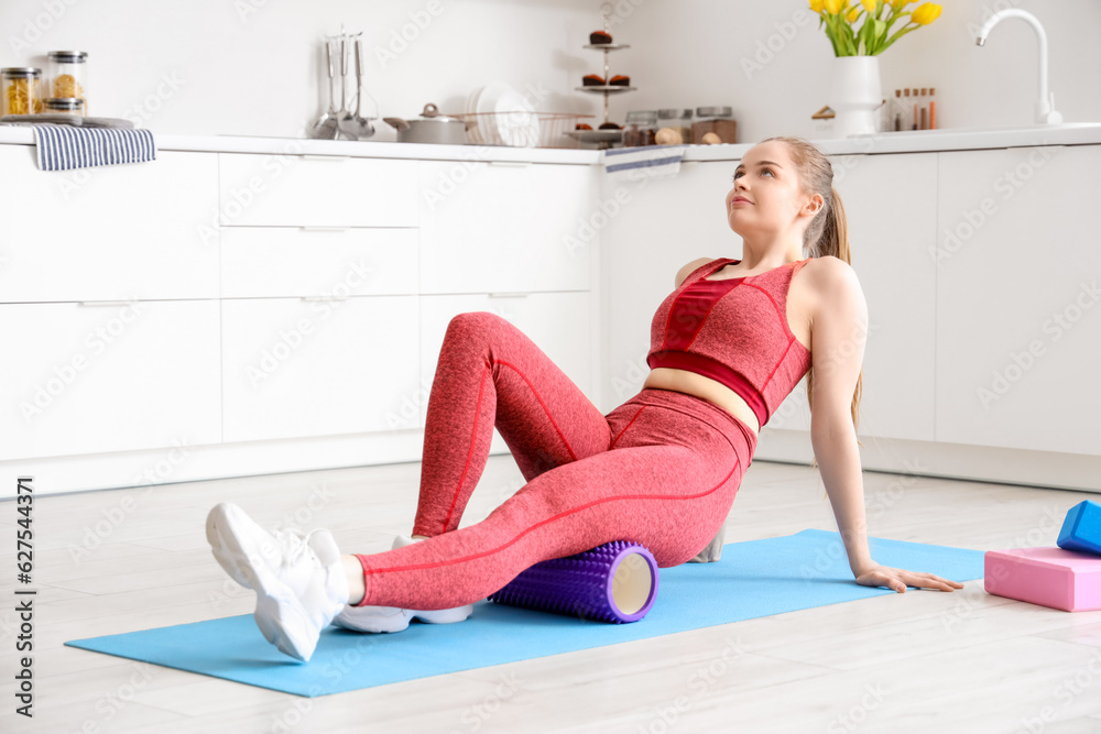 Sporty young woman exercising on yoga mat in light kitchen