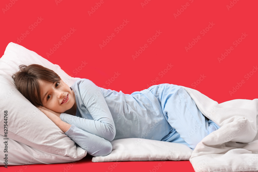 Little boy with pillow and blanket on red background