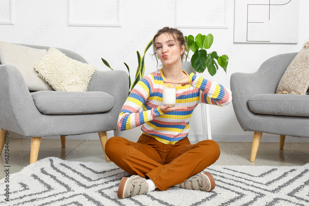 Young woman with glass of milk blowing kiss at home