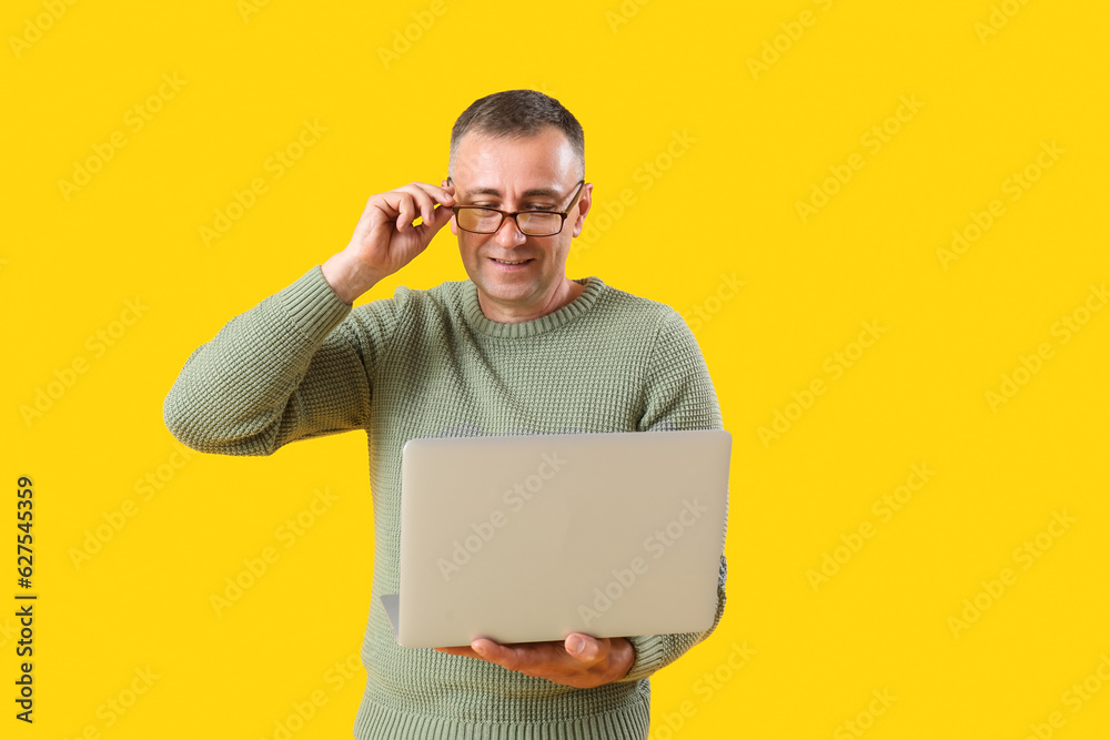 Mature male programmer with laptop on yellow background