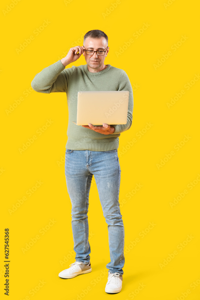 Mature male programmer with laptop on yellow background