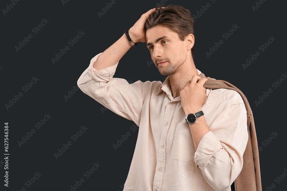 Handsome young man with wristwatch and stylish jacket on black background