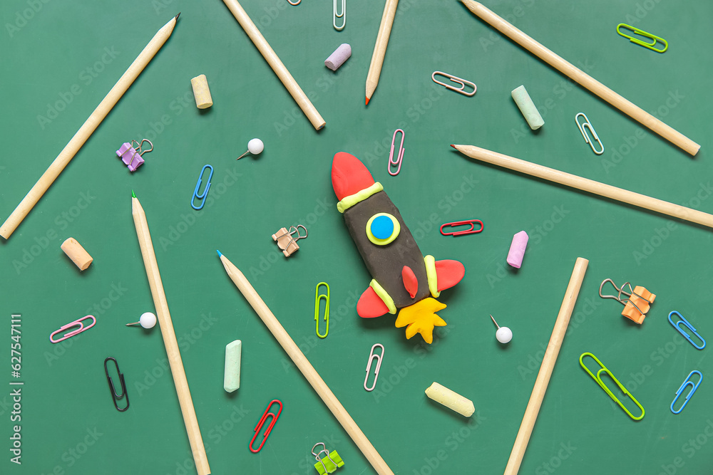 Rocket made of plasticine with different stationery on green chalkboard