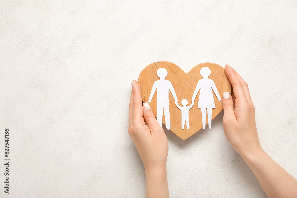 Female hands with wooden heart and figures of family on white background