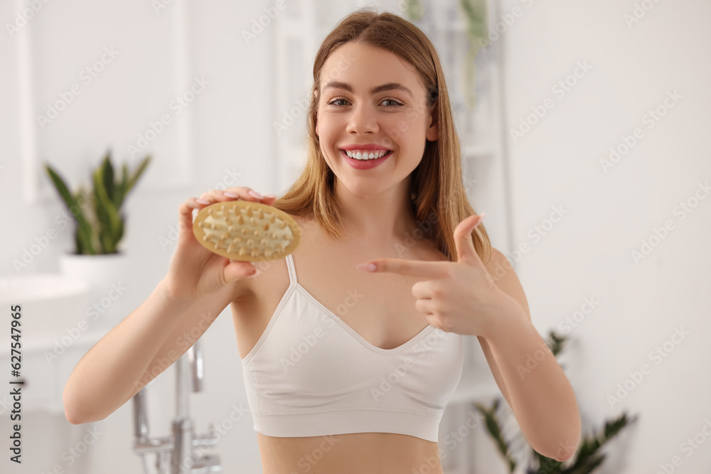 Young woman pointing at anti-cellulite brush in bathroom