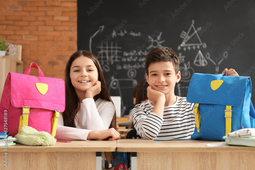 Little pupils with backpacks sitting in classroom