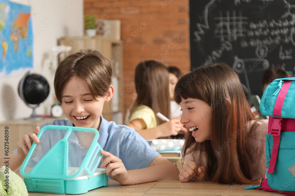 Little pupils with backpack and lunchbox sitting in classroom