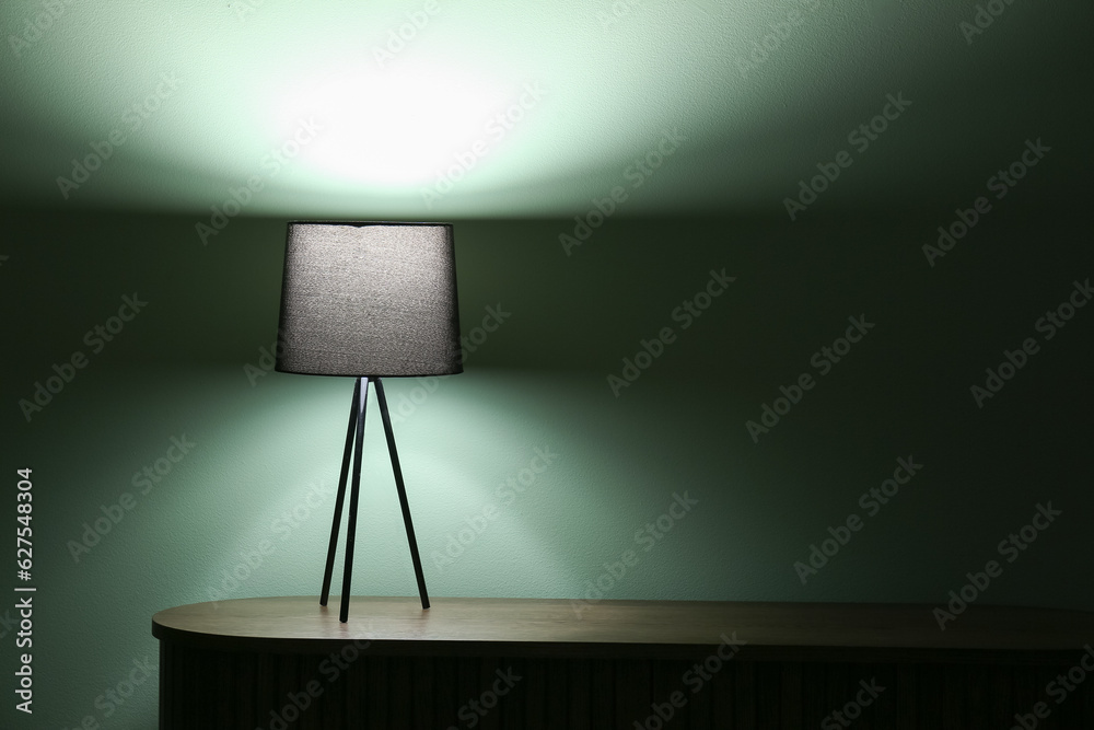 Glowing lamp on wooden table in dark room