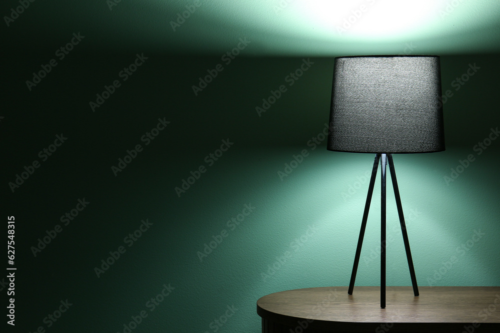 Glowing lamp on wooden table in dark room