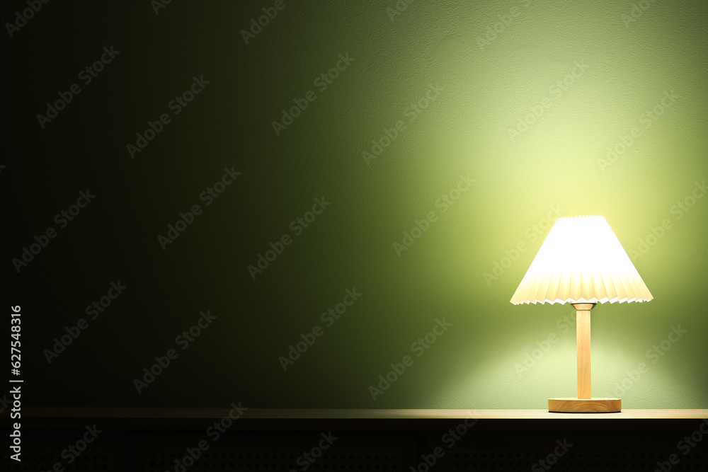 Glowing lamp on wooden table in dark room