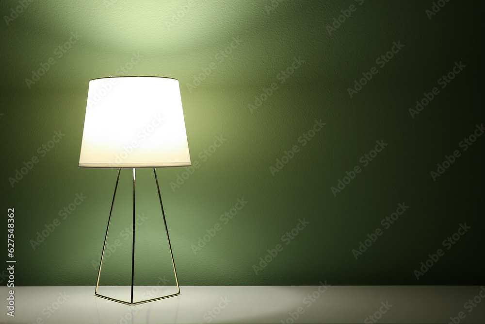 Glowing lamp on table near green wall in dark room