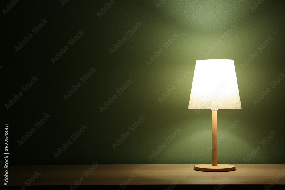 Glowing lamp on wooden table in dark room