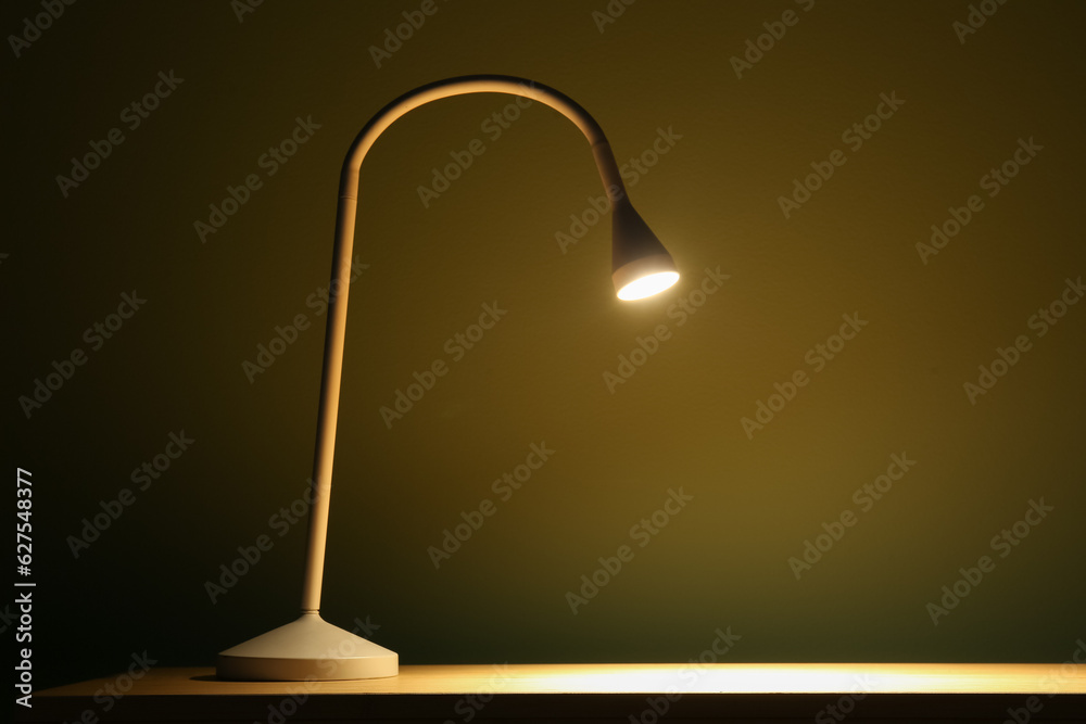 Glowing lamp on wooden table in dark room