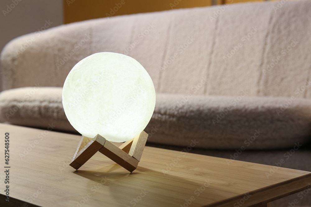 Glowing lamp in shape of moon on wooden table in living room, closeup