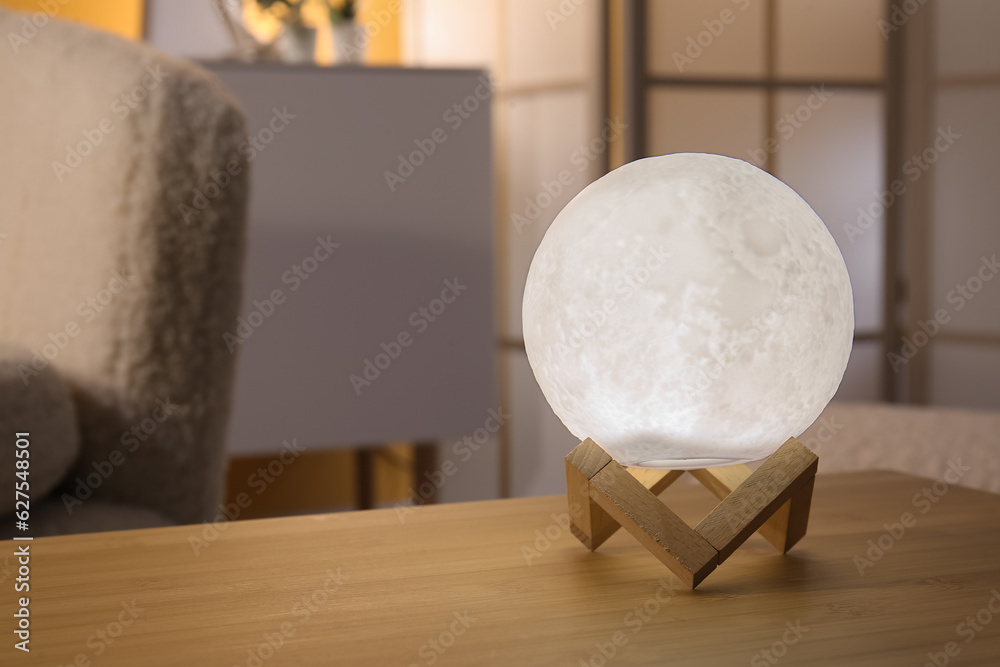 Glowing lamp in shape of moon on wooden table in living room, closeup