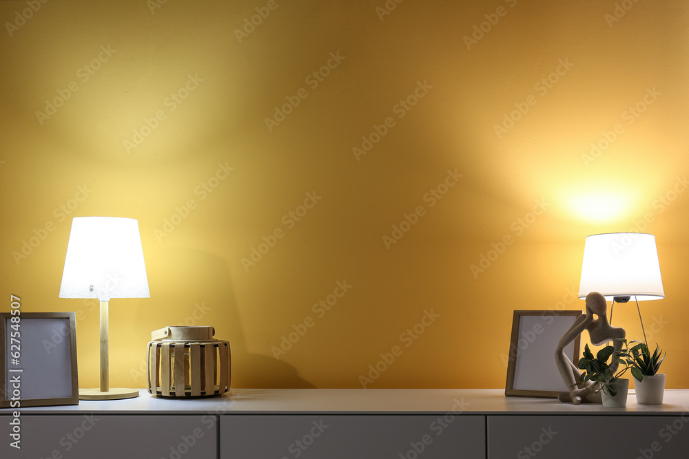 Glowing lamps, blank frames and decor on cabinet in dark room